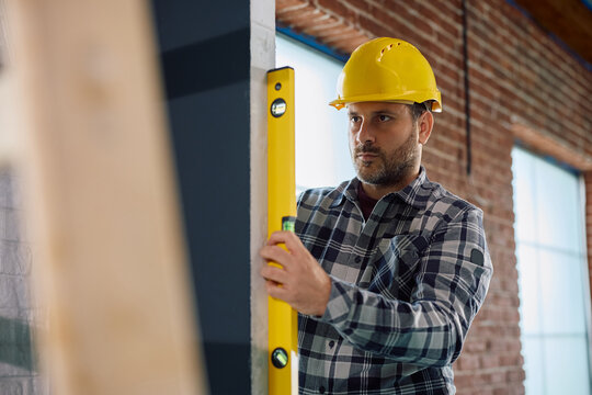 Construction worker using level while wall straightness on site.