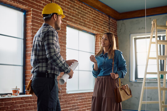 Happy homeowner talking to building contractor at her renovating home.