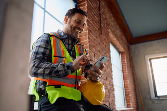 Happy construction site foreman texting on cell phone.