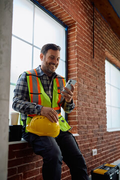 Happy manual worker using smart phone on site.