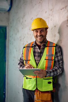Happy construction site foreman using digital tablet while working on home renovation project and looking at camera.