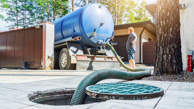 Septic tank service truck connected to sewage tank during daytime work in residential area