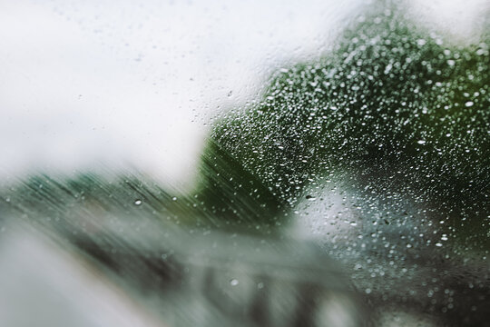 Car windshield glass covered in heavy water droplets with a fast moving wiper blade clearing a smear path during a severe rain storm