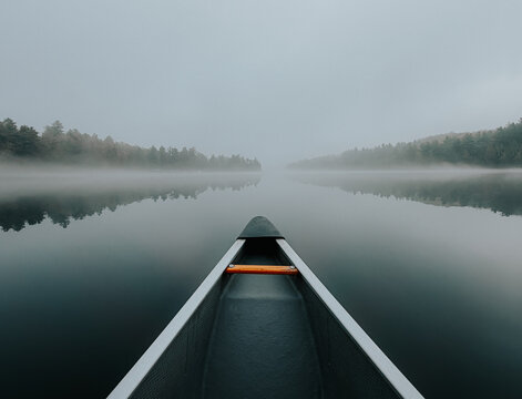 Canoe gliding through fog on a still lake with shoreline in background
