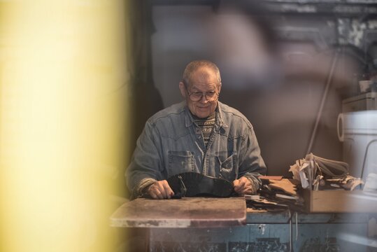 Senior shoemaker smiles while working in workshop
