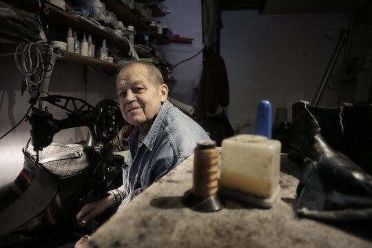 Elderly shoemaker pauses for a portrait in his workshop