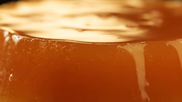 Extreme close-up of glossy amber jelly or flan dessert texture, showing smooth, reflective surface detail of the rich caramel pudding.