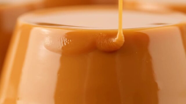 Luxurious close-up of thick, viscous caramel sauce dripping down the side of a shiny custard dessert like flan or panna cotta, highlighting the smooth texture and rich amber color.