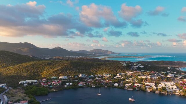 Drone aerial view of Oyster Pond bay on the border of Sint Maarten and Saint Martin. Tropical island landscape features luxury coastal houses and boats anchored in the calm harbor.