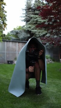 Vertical screen paparazzi sneaks across a garden lawn under a makeshift cover while filming a target with camera gimbal creating a humorous covert surveillance scene