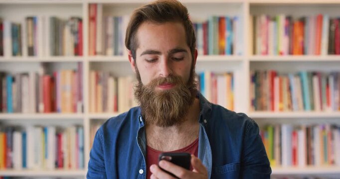 Man, phone and student in library with texting at college by bookshelf, education and search on web. Person, happy with mobile app or tech, assessment and notes for project at university campus
