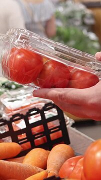 Customer choosing packaged tomatoes in supermarket, hand holding fresh vegetables in plastic container, grocery shopping and healthy food selection concept.