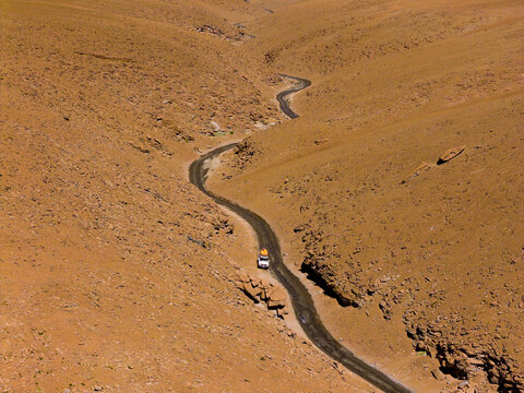 Aerial view of a winding dirt road through the rugged terrain of Canon de las Vizcachas with a white vehicle in the arid landscape in Nor Lipez, Departamento de Potosi, Bolivia.