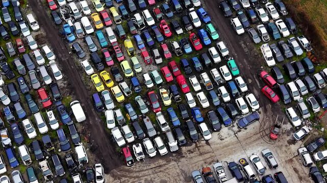 Top-down view of colorful damaged cars in scrapyard, Bulgaria. Aerial drone perspective showing multicolored wrecked vehicles tightly arranged in diagonal rows on gravel and grass.