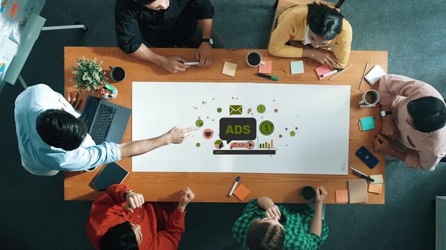 A diverse team collaborates in a modern office setting, discussing advertising strategies with laptops and colorful stationery on a wooden table. Raster