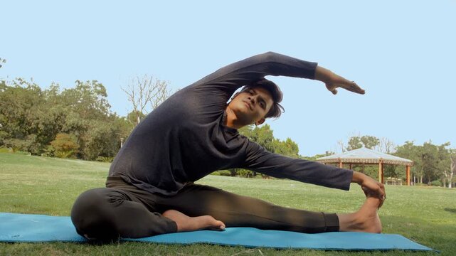 Young boy doing daily workout exercise in the morning - healthy lifestyle  . Medium shot of a young athlete practicing stretching exercises while touching his toes sitting on a mat 