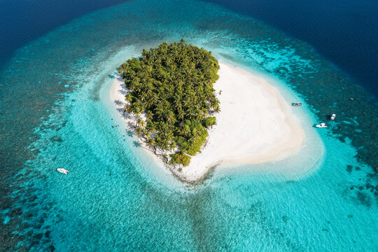 Aerial view of a tropical island with white sand beaches and lush palm trees surrounded by turquoise coral reefs and deep blue ocean water Kudahuvadhoo, Dhaalu Atoll, Maldives.