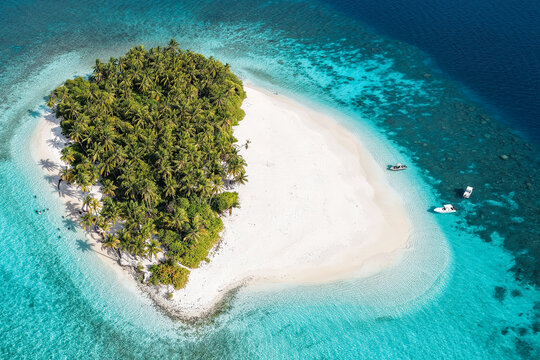 Aerial view of a small tropical island with lush palm trees, white sandy beaches, and turquoise coral reefs surrounded by deep blue ocean water Kudahuvadhoo, Dhaalu Atoll, Maldives.