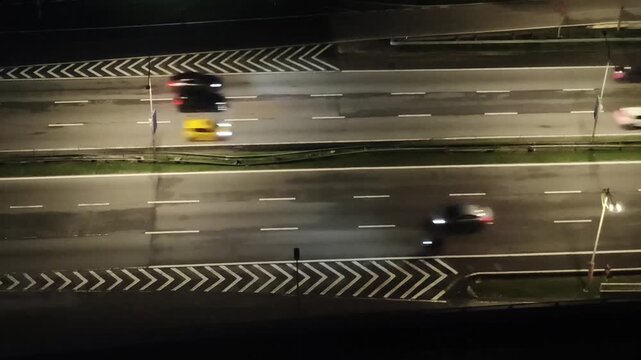 A fast motion video of urban traffic and subway trains blurs through the night city as cars speed along the illuminated street.