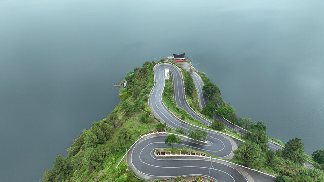 Aerial view of the winding serpentine road of Sibea Bea on a lush green hill overlooking Lake Toba in Samosir Regency, North Sumatra, Indonesia.