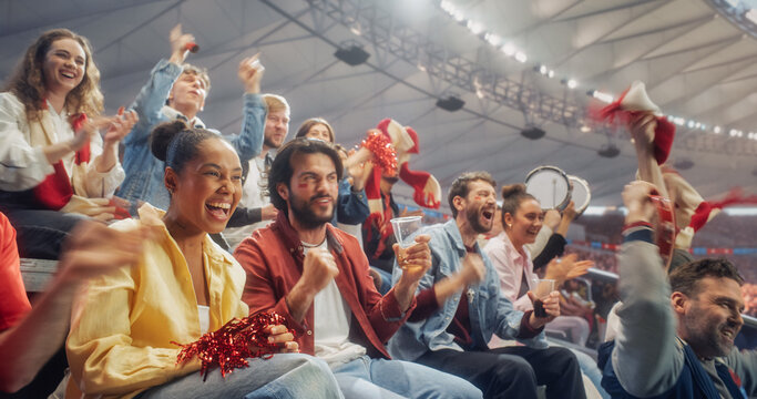 A Black Woman in Yellow and a White Man With Red Cheek Paint Cheer With Soccer Fans From Stadium Seats, Waving Scarves as Nearby Supporters Beat Drums in a Championship Match.