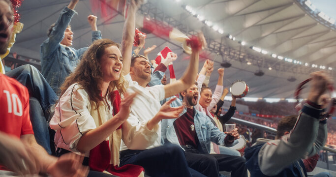 Portrait of Smiling Female Supporter Claps as Nearby Soccer Football Fans Lift Scarves, Beat Drums and Throw up Their Arms to Celebrate a Championship Score Inside a Bright Indoor Stadium.