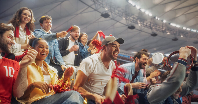 Diverse Fans at a Soccer Football Championship Laugh, Shout and Clap in Stadium Seating After a Crucial Moment, Waving Red Scarves and a Tambourine as Relief and Joy Spread Across Their Faces.