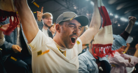 Naklejka premium Close Portrait of White Male Soccer Football Fans in Championship Stadium Stands, Arms and Scarves Raised to Cheer, Happy, Smiling, Excited as Red and Gold Confetti Falls During a Cup Match.