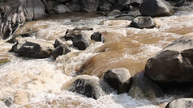Powerful brown water torrent surges through wild river rock formations, creating rapid stream flow, dynamic muddy current and splashing flood rapids with intense energy