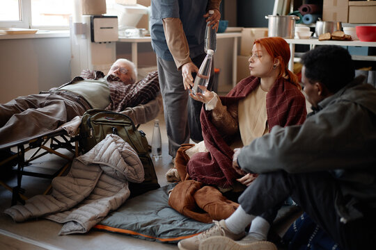 Diverse adults receiving water and resting in humanitarian aid center, supporting displaced people during crisis response. Useful for relief services, shelter support, social care campaigns