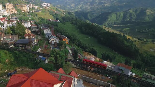Overhead panning shot of the mountain tram as it departs from Sapa town in the late afternoon, aerial wide view