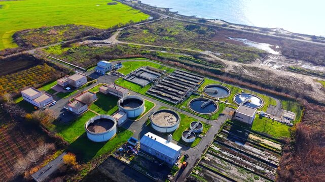 Wide elevated perspective showing industrial processing facility situated along the coastal zone and green fields. Drone shot of water purification infrastructure near Pomorie, Bulgaria.
