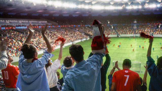 Back View of Diverse Excited Men and Women Waving Red Scarves and Pom-poms, Clapping Hands to Cheer Their Favorite Team Playing on the Pitch, Happy Soccer Fans at a Football Championship Stadium.