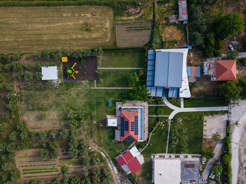 Aerial view of a modern property with solar panels, a colorful playground, and green gardens surrounded by olive groves in Zvernec, Vlore County, Albania.
