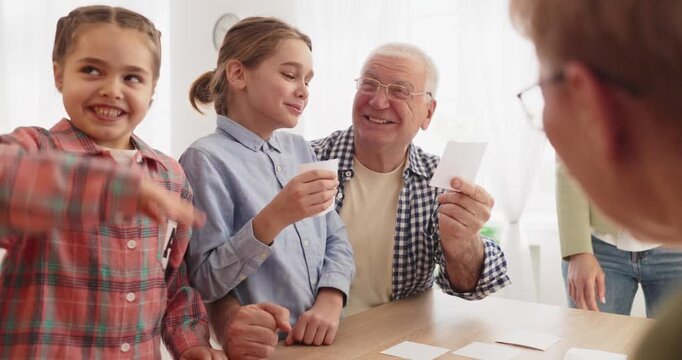 Family children grandparents adults boardgame learning. They laugh at the table, matching memory cards and building education skills in bright indoor light. Joyful family learning and bonding.