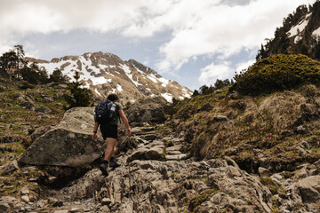 Male hiker with backpack walking along a rocky mountain trail surrounded by pine trees and alpine vegetation in the Spanish Pyrenees. Adventure travel, hiking and outdoor recreation  © aitor