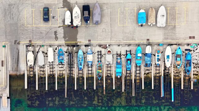 Watercraft parked on ramps and trailers next to vibrant turquoise sea. Row of boats on slipways and parking lot, Pomorie, Bulgaria.