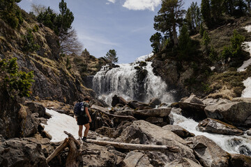 Male hiker standing on rocks in front of a powerful mountain waterfall in the Spanish Pyrenees. Inspiring outdoor adventure scene representing freedom, exploration and connection  © aitor