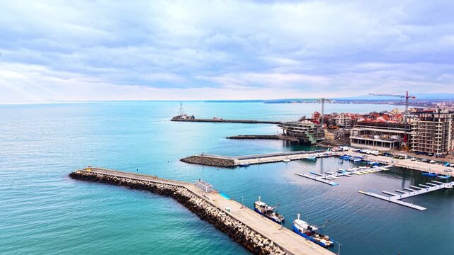 Aerial view of coastal city marina with breakwaters, floating docks and building construction. Modern harbor development and stone piers, Pomorie, Bulgaria