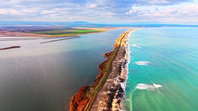 Panoramic aerial view of thin land strip dividing turquoise ocean water from dark inland lagoon. Narrow sand spit separating sea from lake, Pomorie, Bulgaria.
