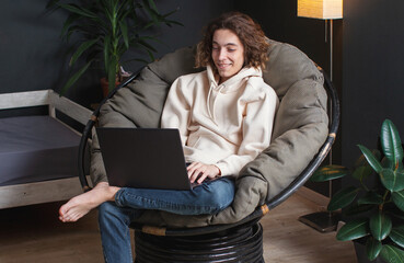 Fototapeta premium Smiling young man sitting on sofa with laptop at home