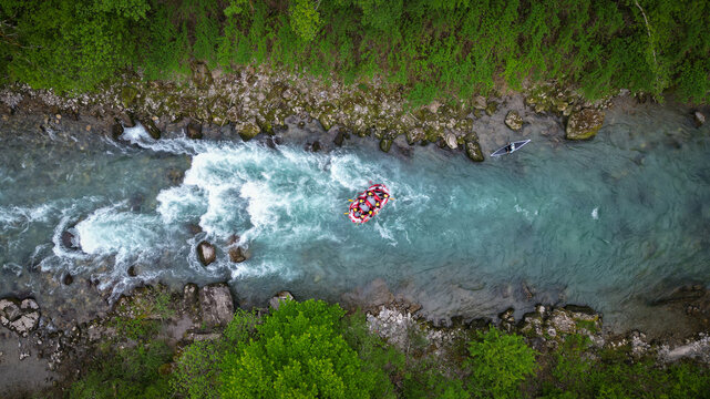 Aerial view of a red rafting boat navigating white water rapids on the Dranse river surrounded by lush green forest and rocky banks, Haute-Savoie, Auvergne-Rhone-Alpes, France.