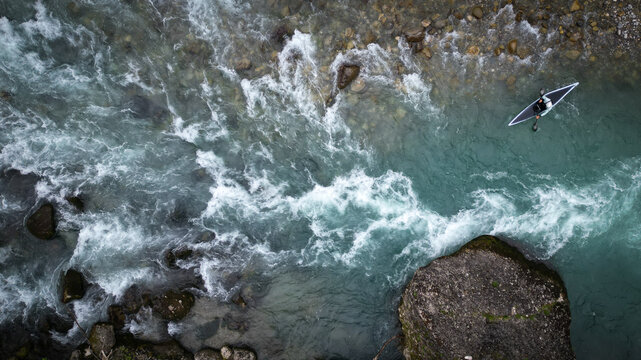 Aerial view of a person in a kayak navigating the white water rapids of the Dranse river with turquoise water and rocky banks in Haute-Savoie, Auvergne-Rhone-Alpes, France.