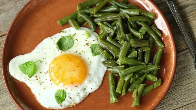 Morning breakfast. Fried egg and prepared green beans garnished with fresh basil leaves on plate