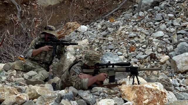 Soldiers practice shooting skills during training at a rocky location in the afternoon sun