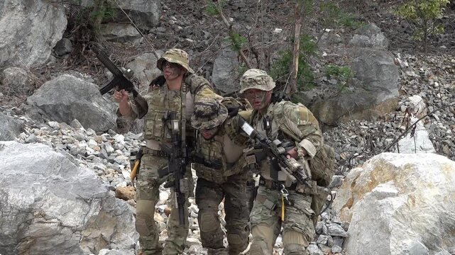 Soldiers help injured comrade in rocky terrain during a training exercise