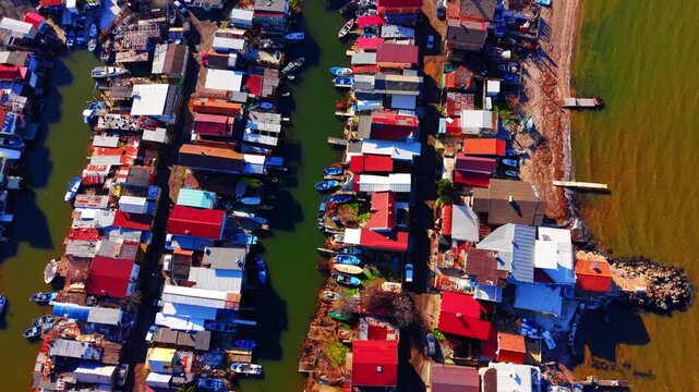 Dense residential roofs lining a narrow water channel. Overhead drone shot of fishing settlement canals.