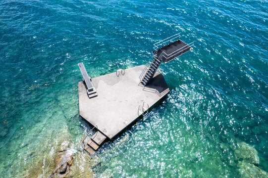 Aerial view of a hexagonal concrete diving platform with stairs and diving boards in the clear turquoise water of Lake Geneva in Lutry, Vaud, Switzerland.