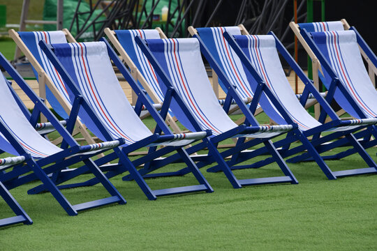 Empty blue and white deck chairs arranged in rows on green turf at an outdoor event. Sun-ready seating evokes summer vacation and holidays like Independence Day and Labor Day.