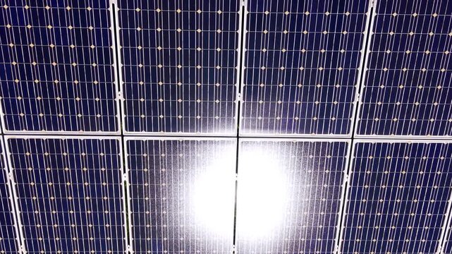 Macro top-down detailed shot of silicon cells showing bright solar reflection on glass surface. Close up of photovoltaic module grid with intense sun flare.